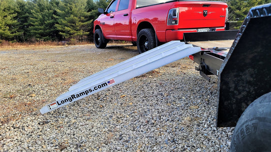 A heavy-duty aluminum loading ramp connected to a black trailer, illustrating the difference in an aluminum vs steel ramp comparison.